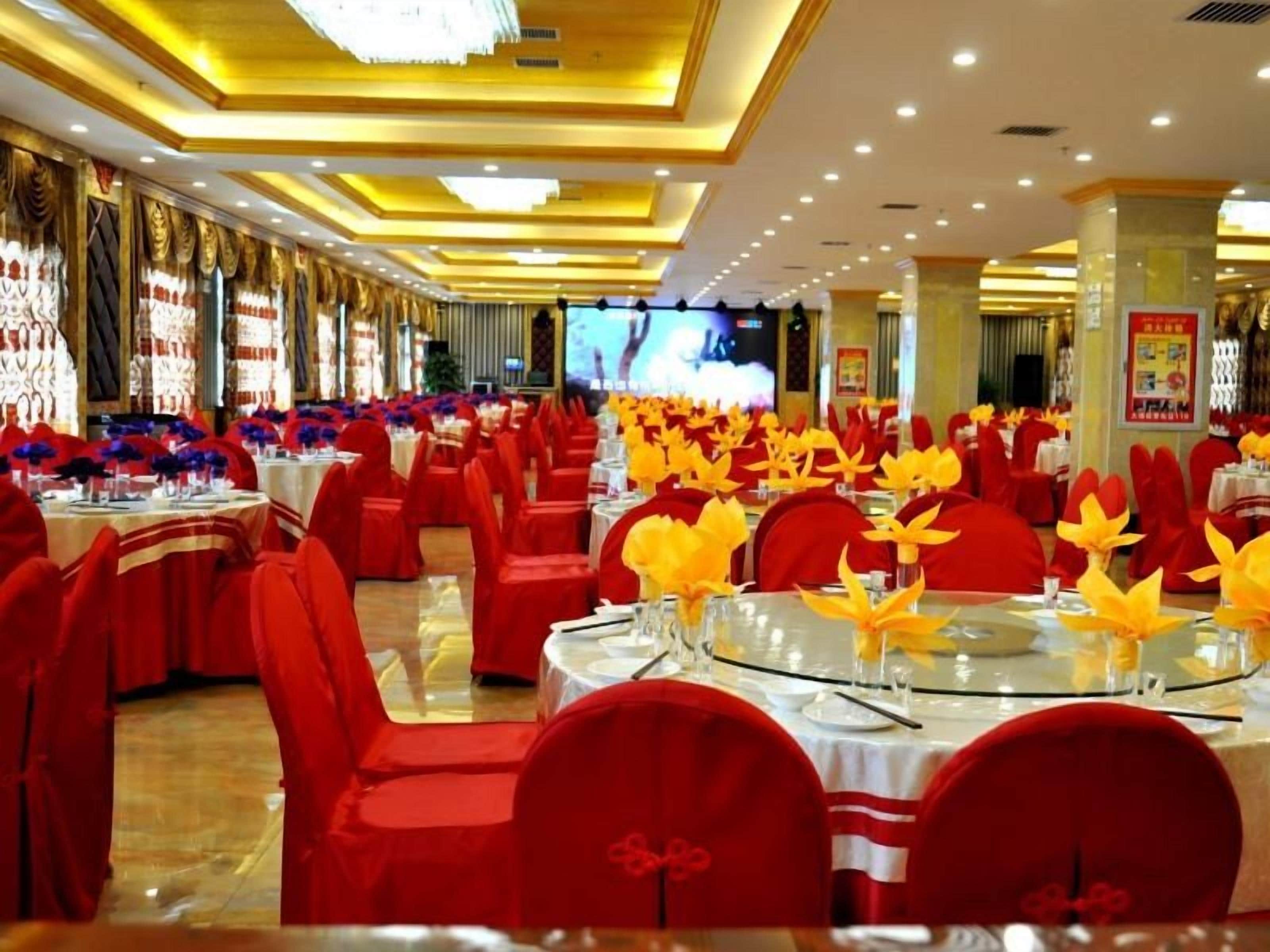 Un salón de banquetes con mesas redondas, sillas rojas y centros de mesa amarillos.