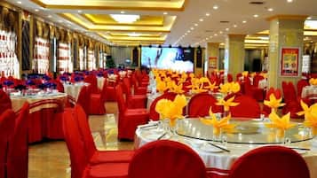 Un salón de banquetes con mesas redondas, sillas rojas y centros de mesa amarillos.