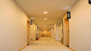 Un couloir d’hôtel avec un sol recouvert de moquette, des portes des deux côtés et des panneaux indicateurs au-dessus de chaque porte.