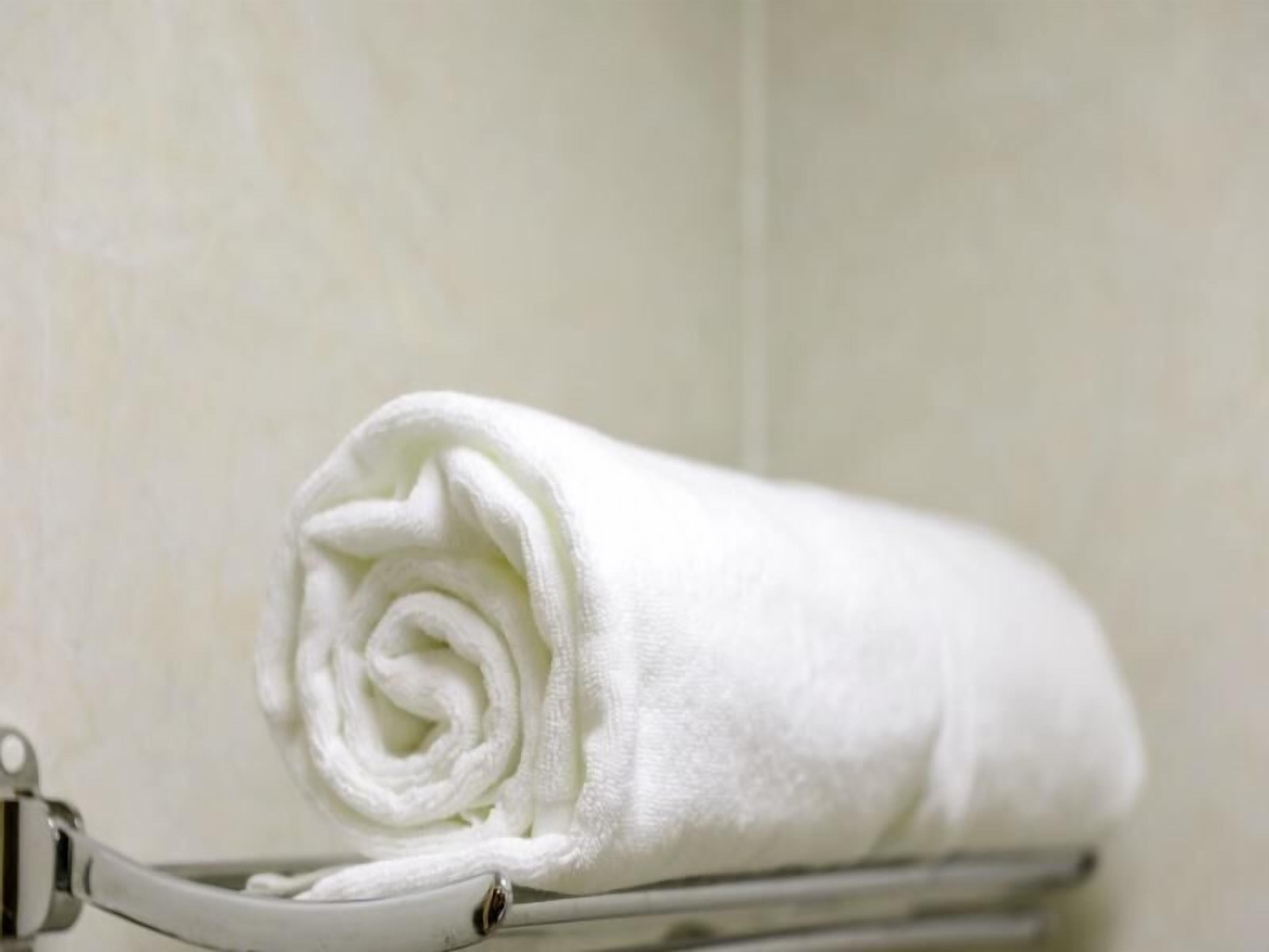 A neatly rolled white towel on a metal towel rack.