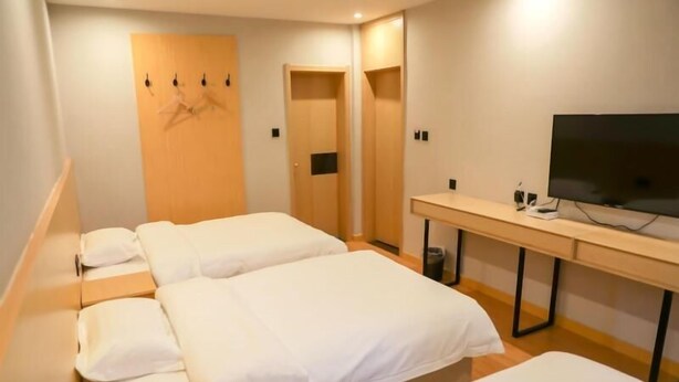 Une chambre d’hôtel avec deux lits simples, un bureau en bois avec une télévision et une armoire en bois avec un miroir.