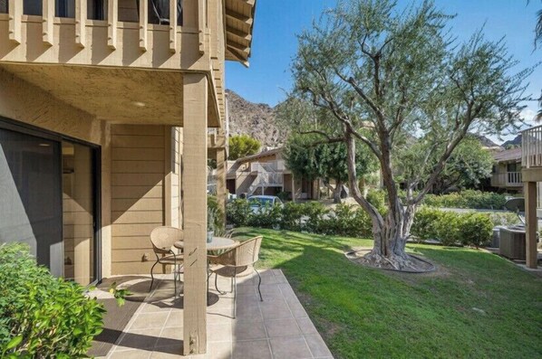 Enjoy outdoor dining or relaxation on the spacious patio with a dining table and two chairs, surrounded by well-maintained landscaping and a mature tree.