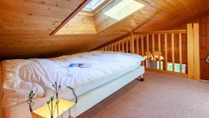 Une chambre avec un plafond en pente et un puits de lumière, des murs en bois, un lit et une petite table avec une lampe.