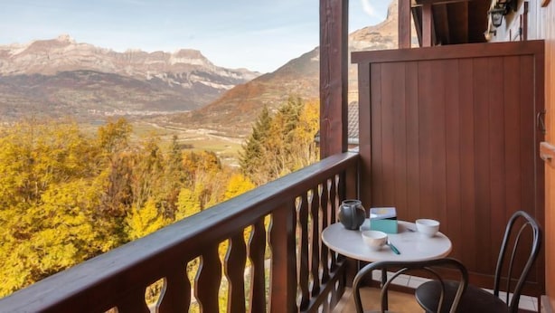 Un balcon avec une table et des chaises, donnant sur un paysage montagneux aux couleurs automnales.