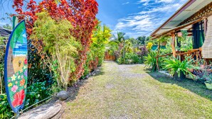 Un chemin menant à un bâtiment doté d’un porche abrité, entouré d’une végétation tropicale luxuriante et agrémenté d’une enseigne décorative.