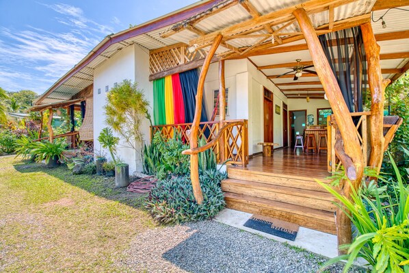 A wooden house with a porch, a welcome mat, and a variety of plants.
