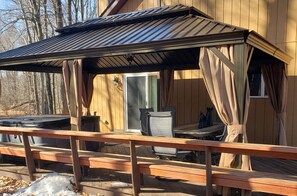 A wooden deck with a covered seating area, a hot tub, and a sliding glass door leading to an interior space. - The Dragon House, Hot Tub, Mini Golf, Pet Friendly (Tobyhanna)