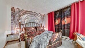 Ein Schlafzimmer mit einem Bett, einem Nachttisch, einer Lampe, einem roten Vorhang und einem Fenster mit Blick auf ein Gebäude.