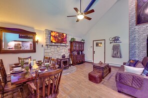 A spacious living room with a stone fireplace, wooden furniture, and a ceiling fan.
