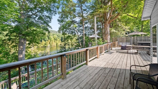 A wooden deck with a view of a lake and trees, a picnic table, and a covered area with chairs. - River Front Home with Amazing views and a shared private island! (Newaygo)