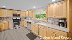 A modern kitchen with wooden cabinets, stainless steel appliances, and a view of greenery outside. - River Front Home with Amazing views and a shared private island! (Newaygo)