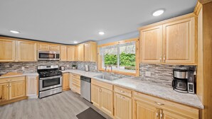 A modern kitchen with wooden cabinets, stainless steel appliances, and a view of greenery outside. - River Front Home with Amazing views and a shared private island! (Newaygo)