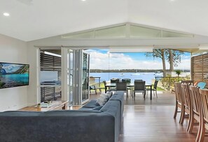A modern living room with a large sofa, dining table, and chairs, a TV, and a view of the sea.