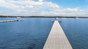 A calm body of water with a wooden dock extending into it, surrounded by boats and a clear sky. - Sunset Central Coast - Lake, Kayaks & Jetty! (Mannering Park)