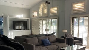 A modern living room with a sectional sofa, a coffee table, and a TV mounted on the wall. - Spacious home in Avondale Golf Club. Available May 1st 2025! (Palm Desert)