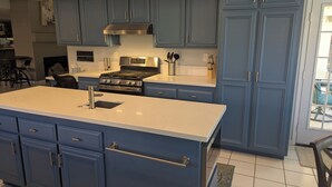 A modern kitchen with blue cabinets, a stainless steel range hood, and a white countertop. - Spacious home in Avondale Golf Club. Available May 1st 2025! (Palm Desert)