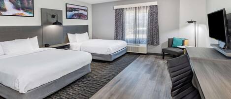A hotel room with two beds, a desk, a television, and artwork on the walls.