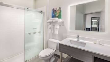 A modern bathroom with a glass shower enclosure, a white toilet, a sink with a mirror, and a towel rack with folded towels.