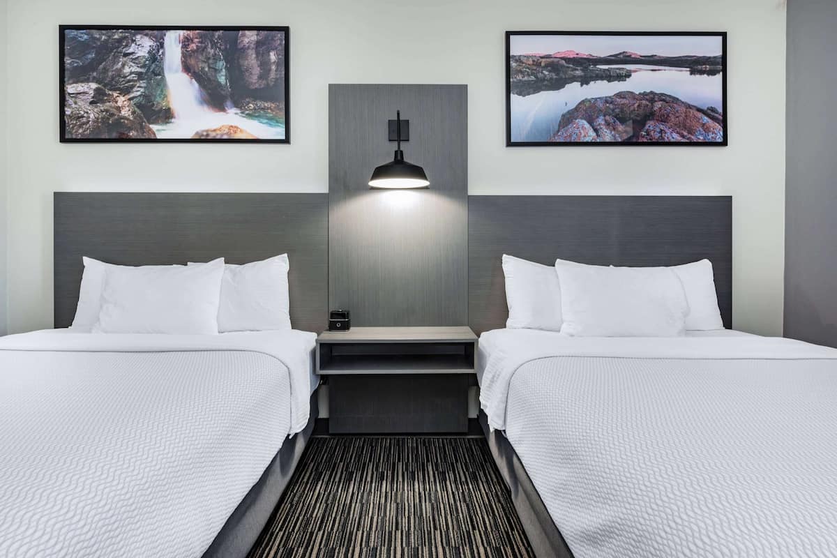 A hotel room with two beds, a nightstand, a lamp, and two framed pictures on the wall.