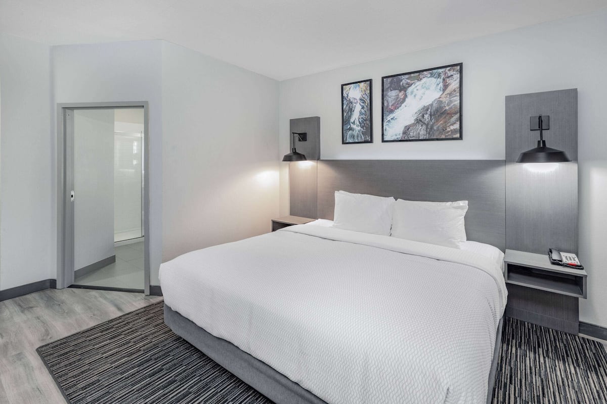 A modern hotel room with a large bed, two bedside tables, a nightstand, and two wall-mounted lamps.