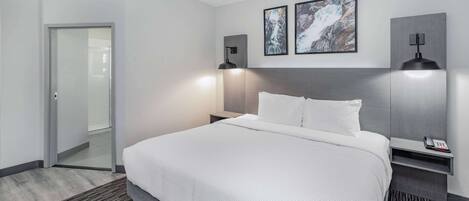 Une chambre d’hôtel moderne avec un grand lit, deux tables de chevet, une petite table et deux lampes fixées au mur.