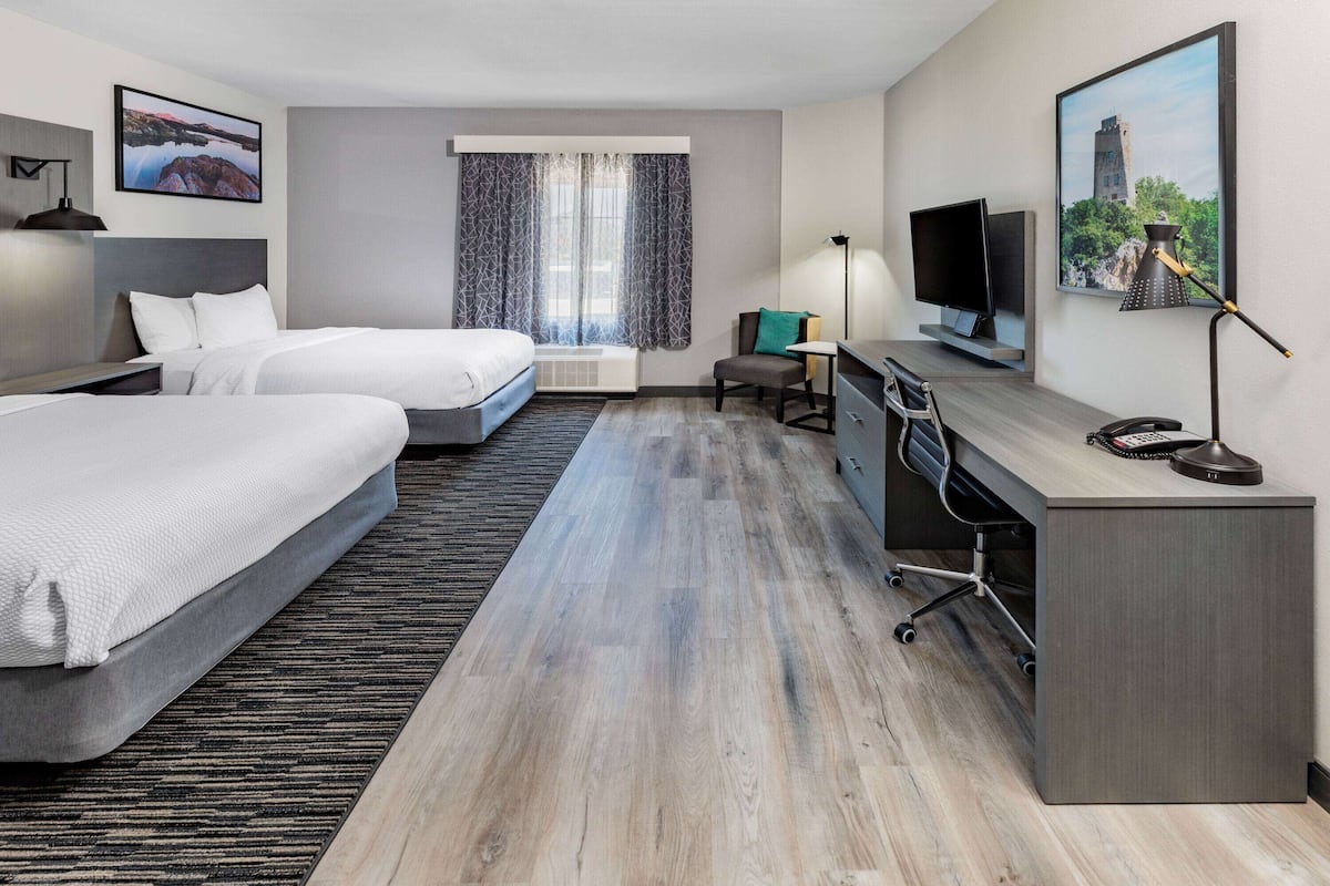 A hotel room with two beds, a desk, a TV, and a window with curtains.