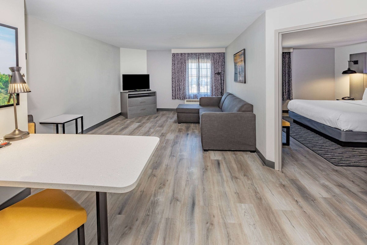 A modern hotel room with a dining area, a sofa, a bed, and a television.