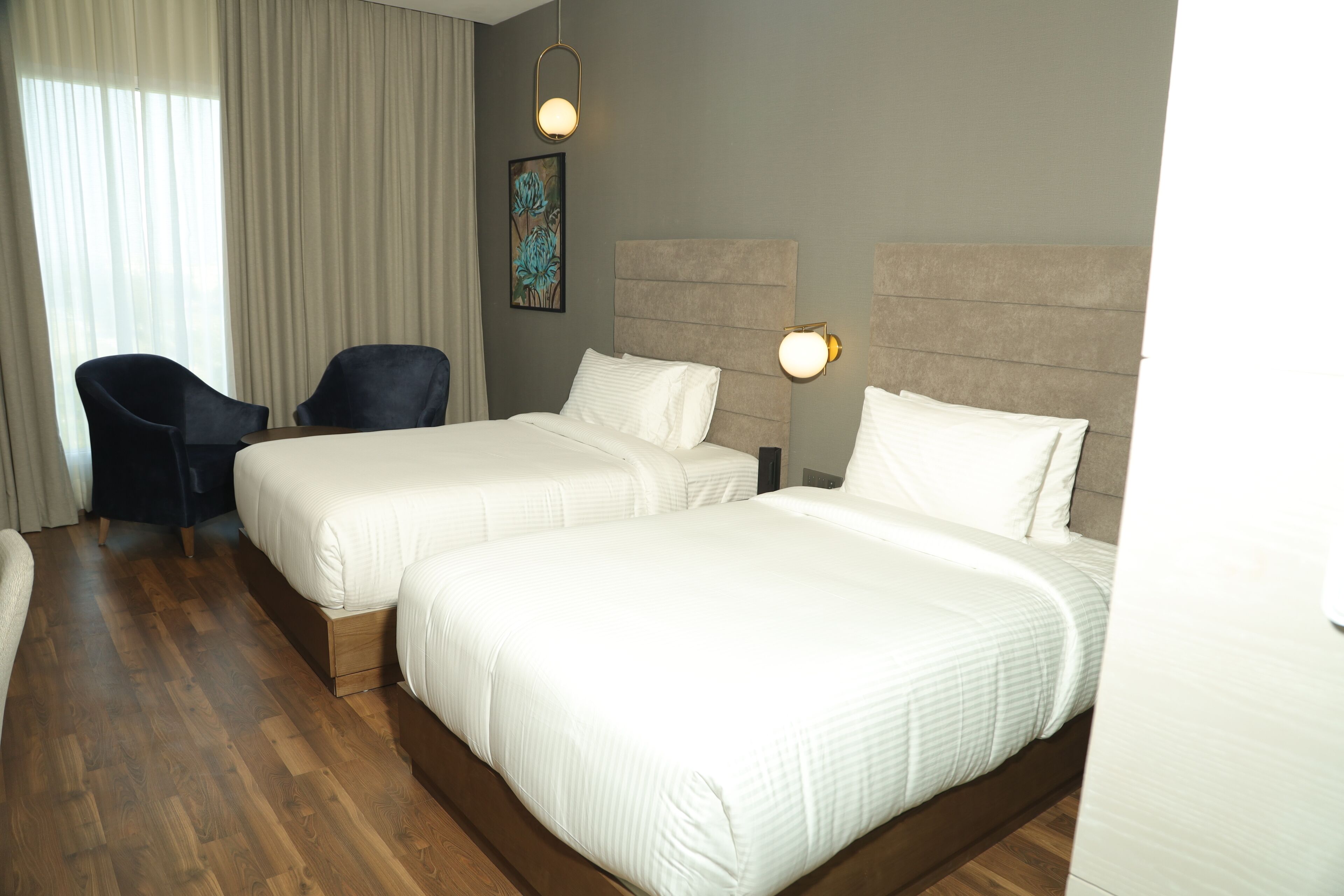 A hotel room with two beds, a chair, and a painting on the wall.