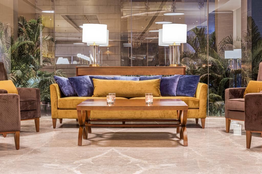 Un hall con un sofá, sillones, una mesa de centro y un ventanal con plantas.