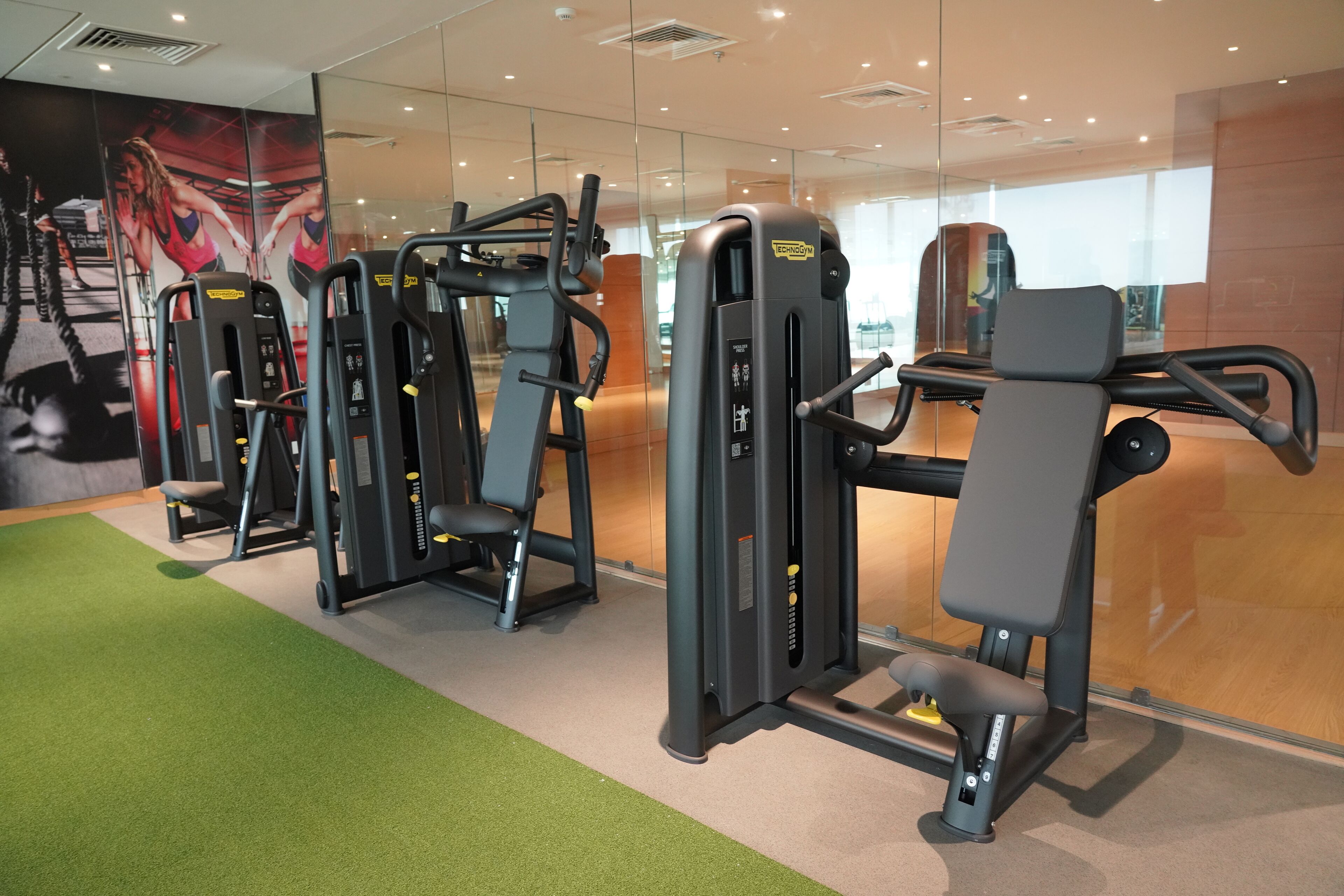 Una palestra con diverse macchine per esercizi, un tappeto verde e uno specchio grande.
