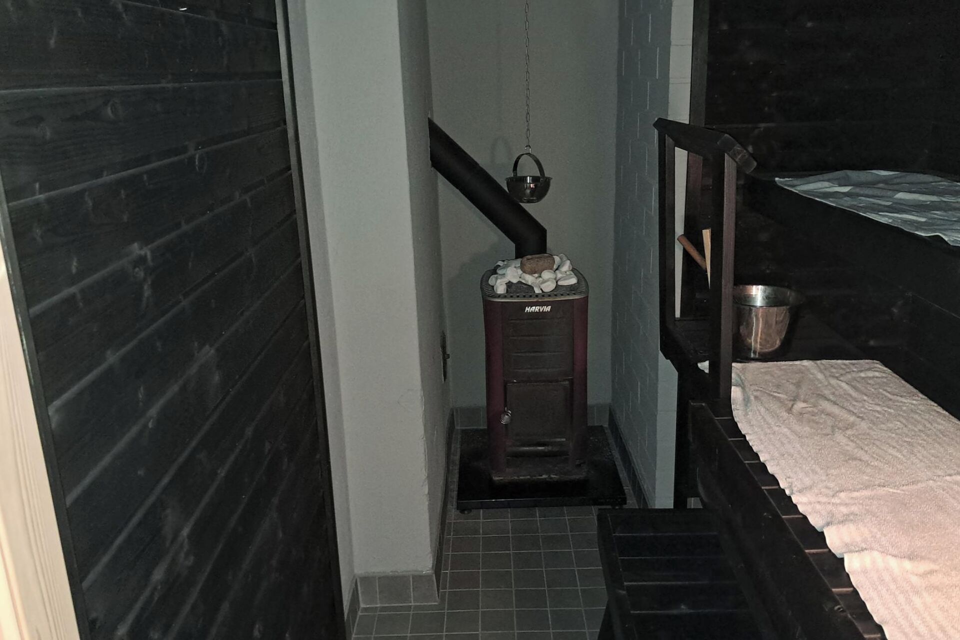 Een kleine kamer met een houtkachel, een metalen emmer en een klein trapje naar een bed.