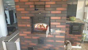 A brick fireplace with a glass door, a small shelf above it, and a kitchen area with a stove and cabinets.