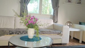 A living room with a white sofa, a glass coffee table, and a vase with flowers.