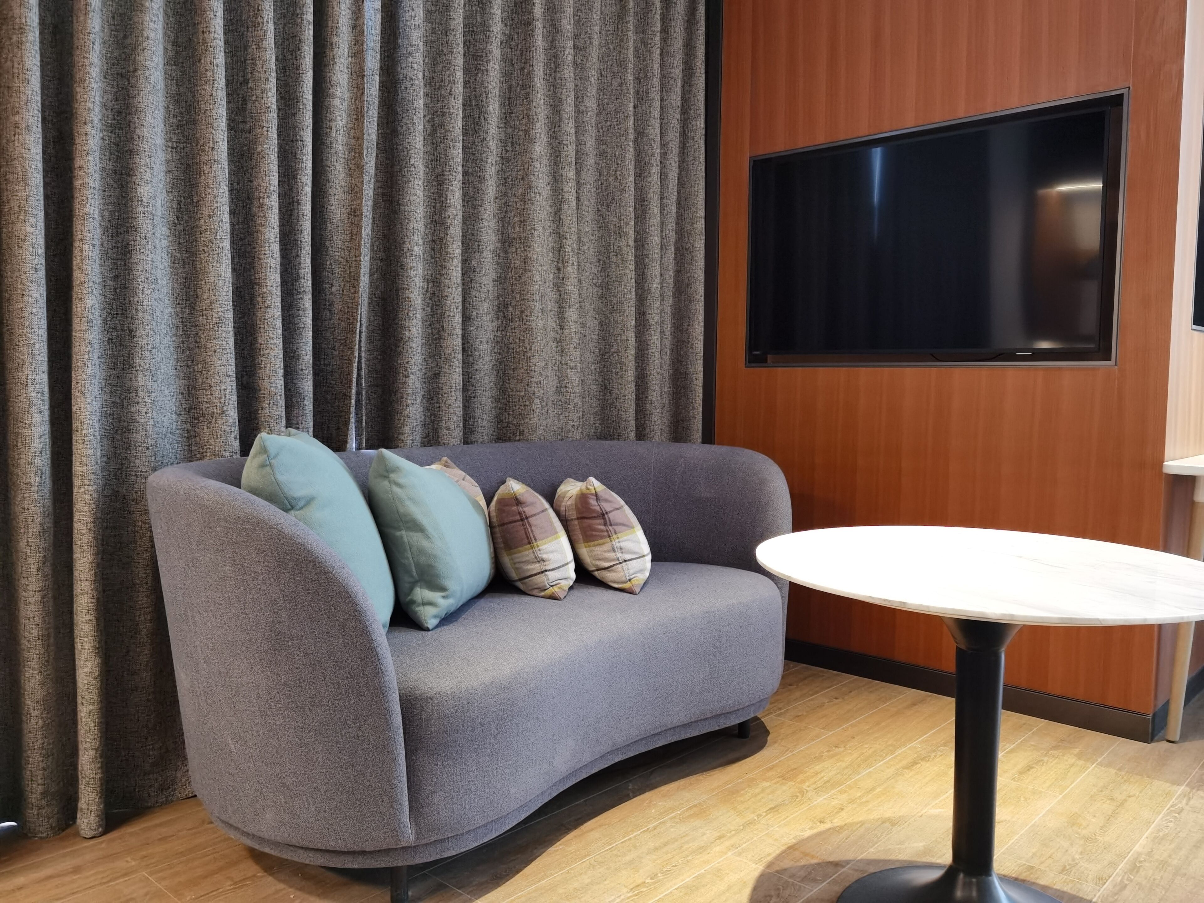 A modern room with a grey sofa, a round table, and a flat-screen TV mounted on a wooden wall.