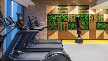 A row of stationary exercise bikes in a gym with a green wall and a punching bag.