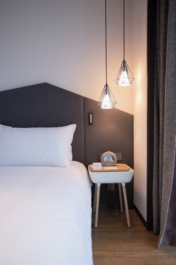 A hotel room with a bed, bedside table, and two pendant lights.