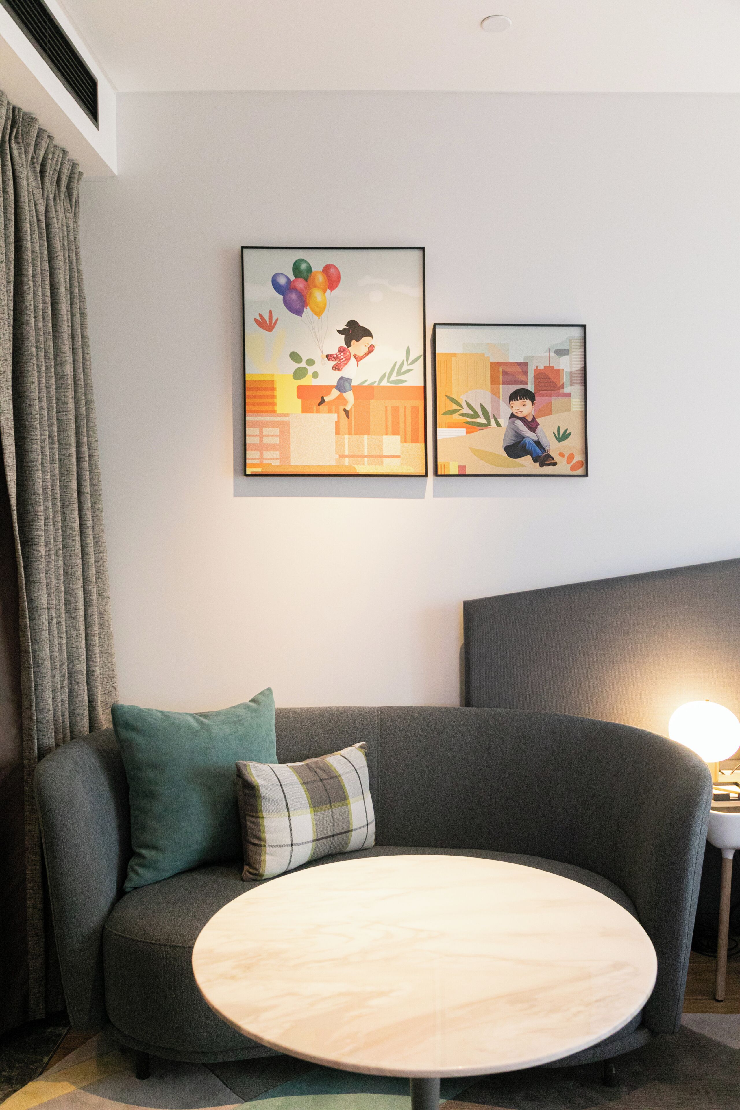 A modern living room with a grey sofa, a round wooden coffee table, and two framed artworks on the wall.