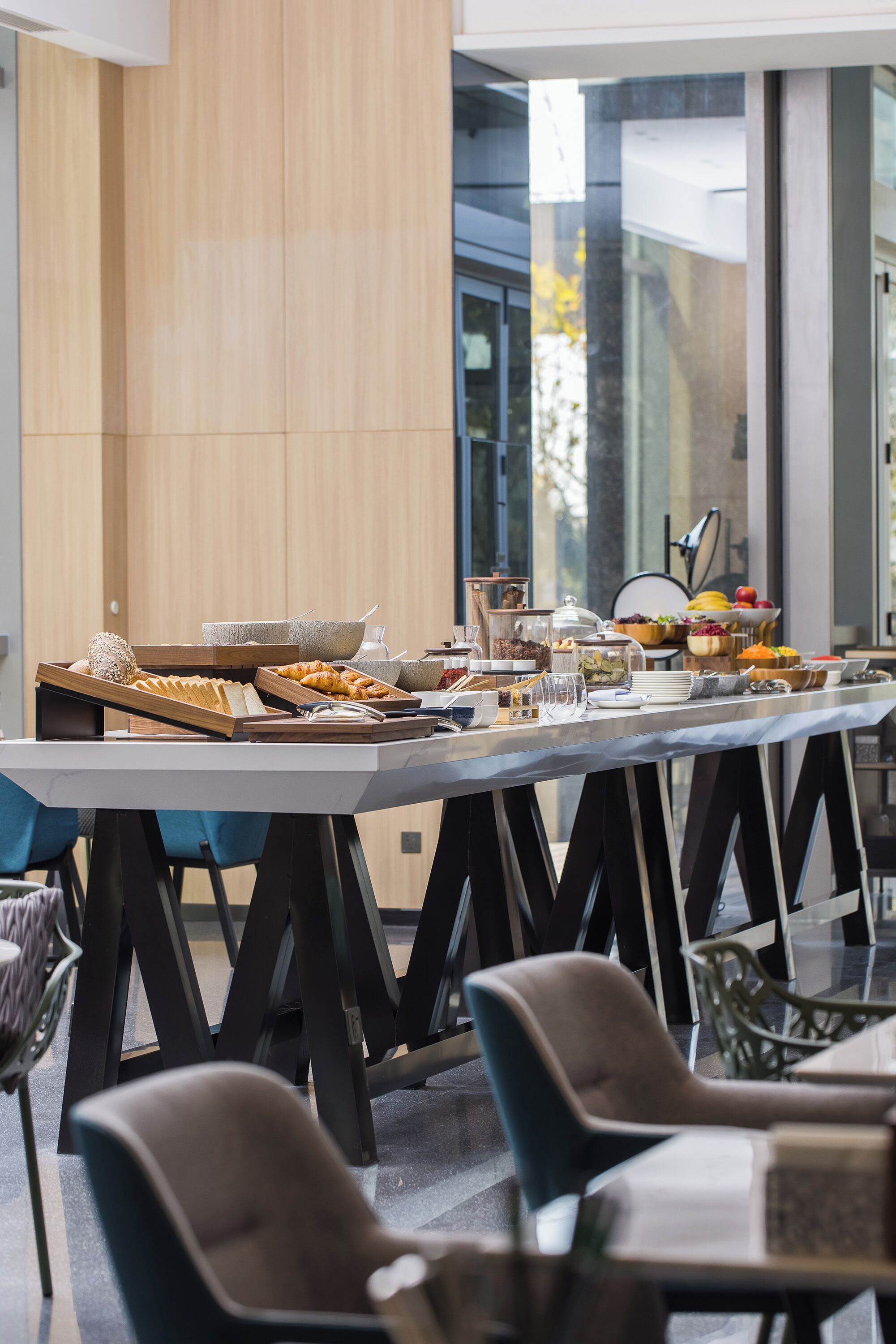 A buffet setup with various food items and glassware on a long table, surrounded by chairs.