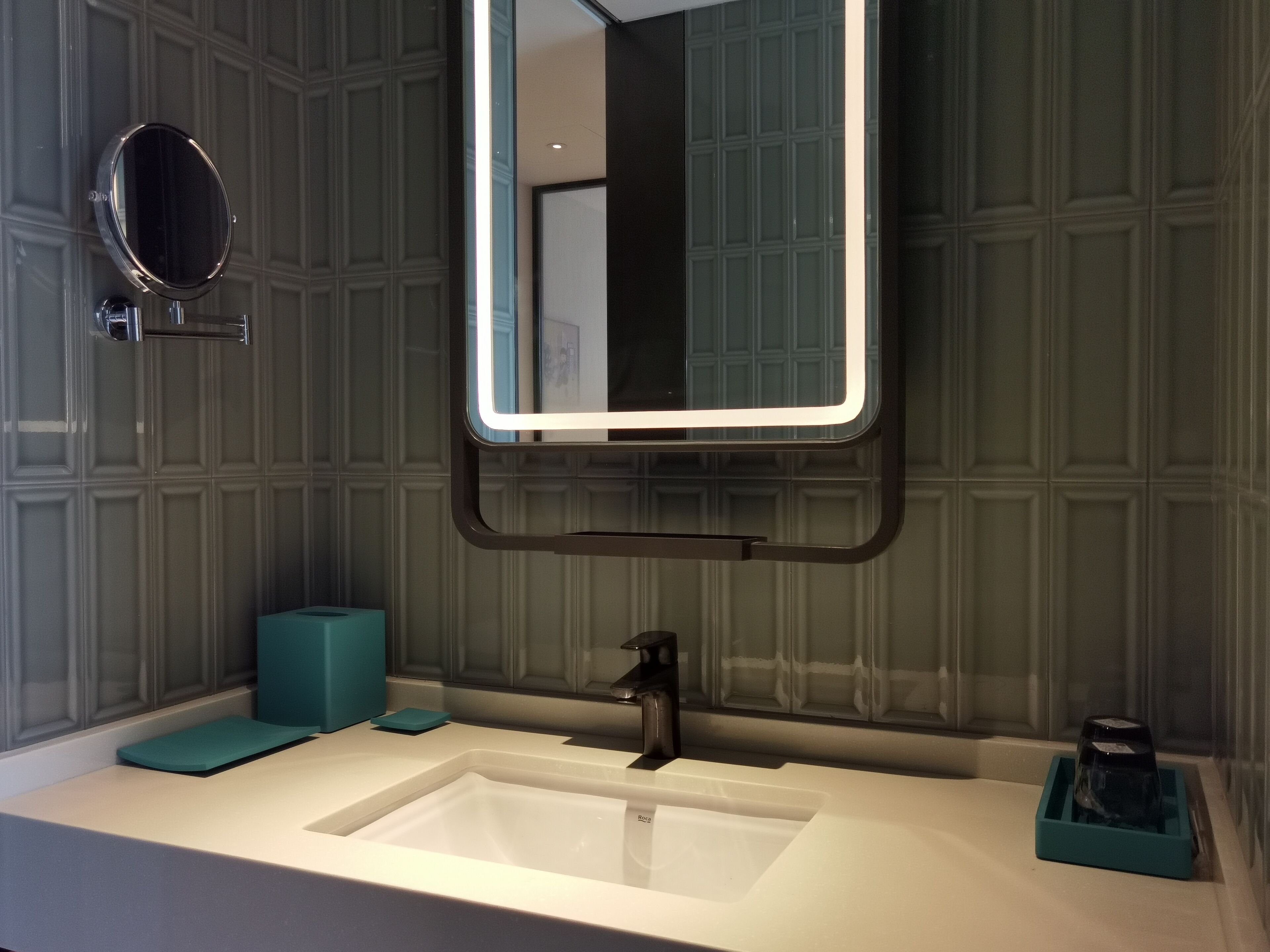 A bathroom with a white sink, a mirror with a light, and a teal soap dish.