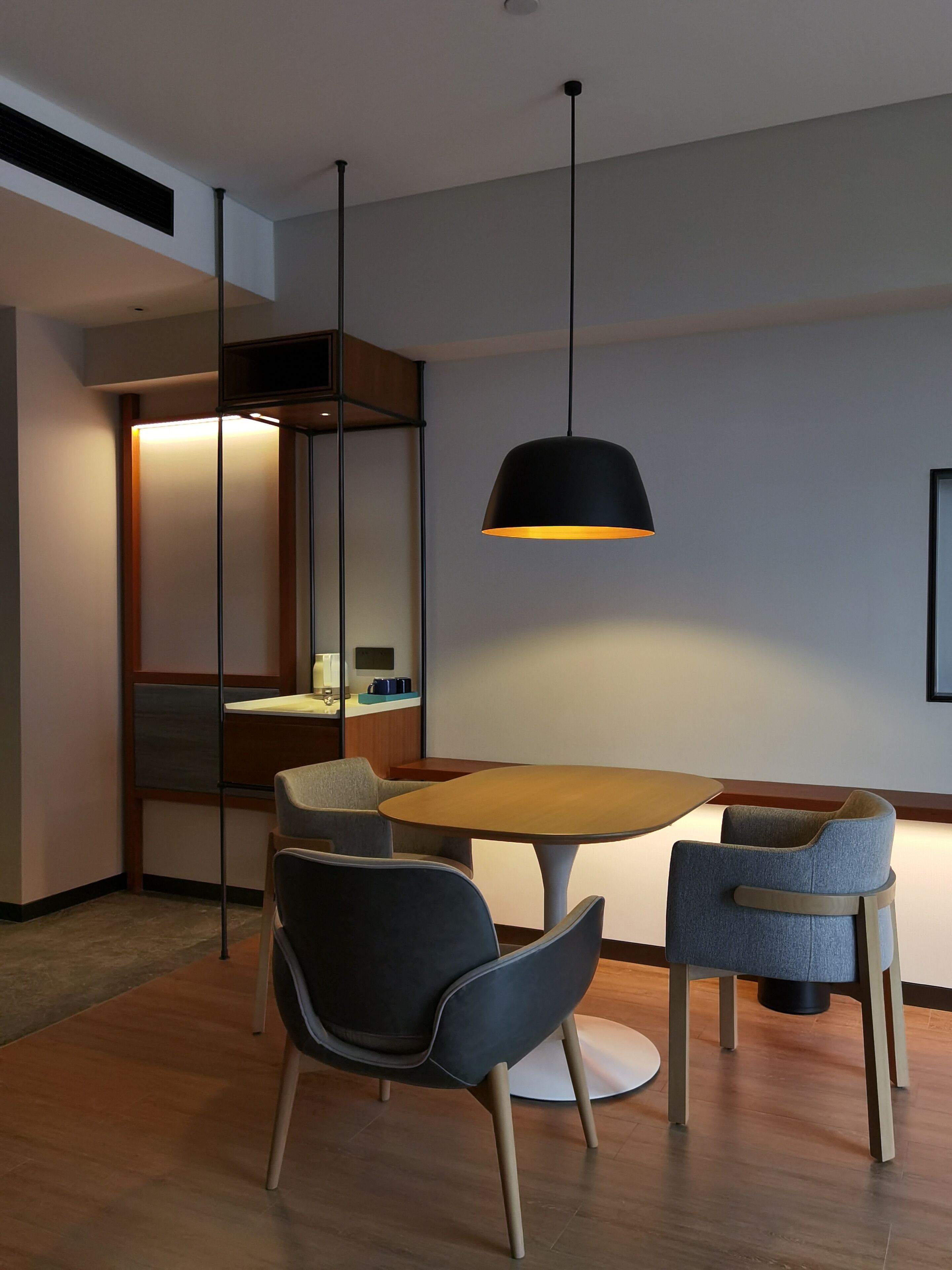 A modern dining area with a round table, two chairs, and a pendant light.