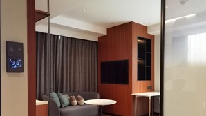 A modern room with a grey sofa, a small round table, a flat-screen TV mounted on a wooden panel, and a digital thermostat on the wall. - Artyzen Habitat Qiantan Shanghai   (Shanghai)