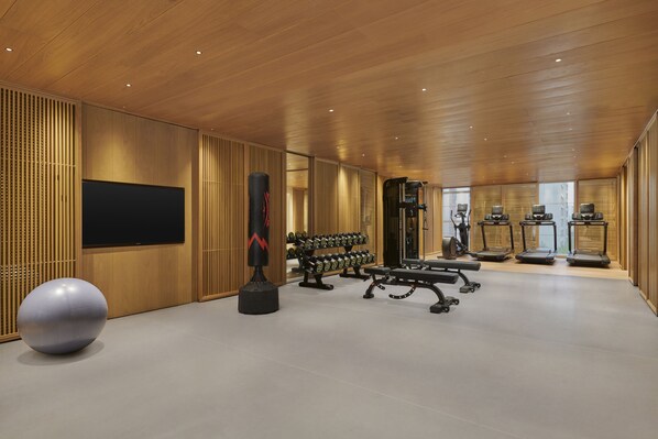 Une salle de sport moderne avec des panneaux de bois, du matériel d’exercice et un grand écran de télévision.