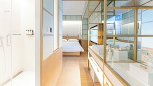 Una habitación de hotel moderna con una cama grande, un baño con cabina de ducha de vidrio y vistas a la ciudad a través de amplias ventanas.
