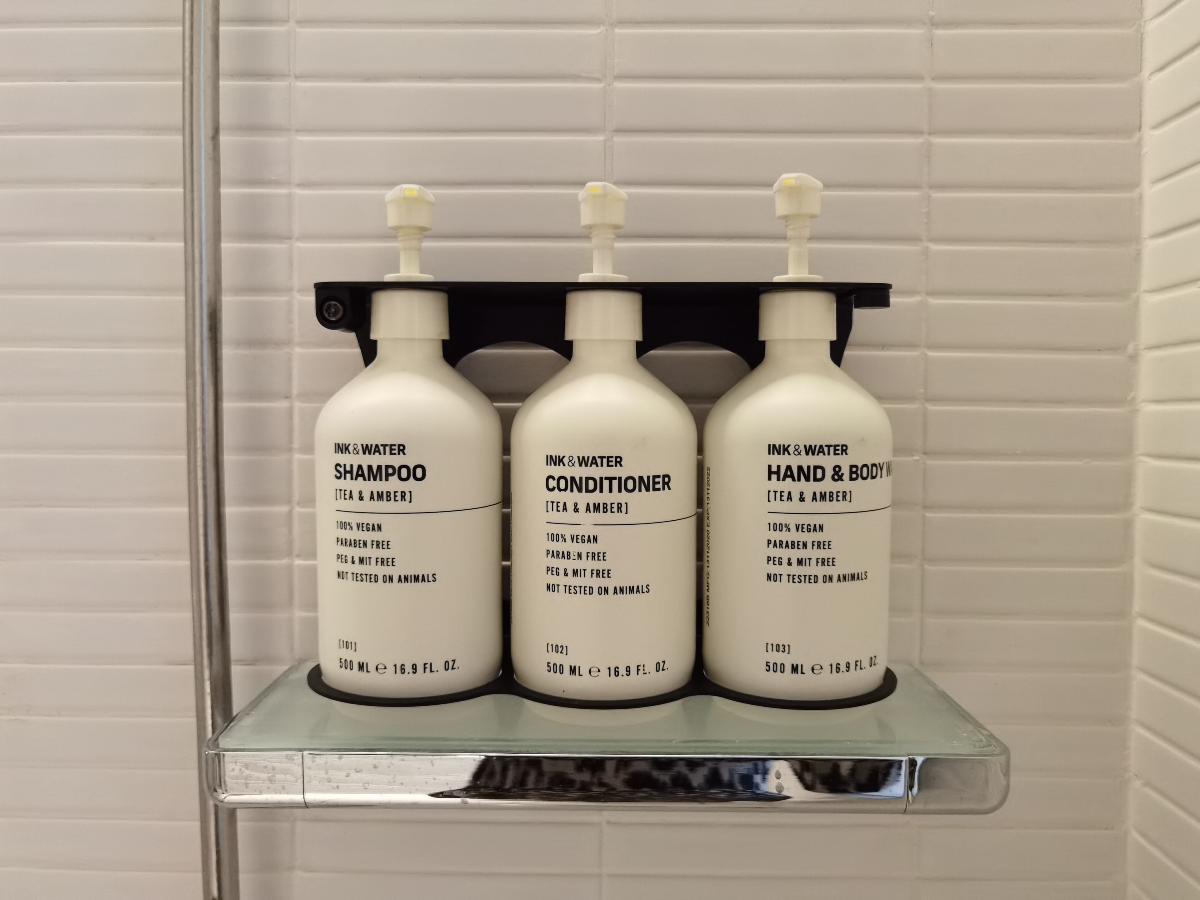 Trois bouteilles de 500 ml de shampoing, d’après-shampoing et de gel pour les mains et le corps, posées sur une étagère.