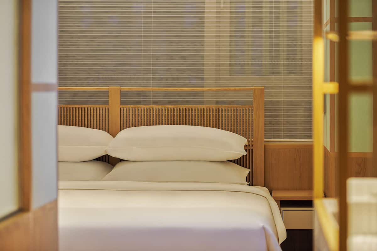 Una cama bien hecha con cabecera de madera, una mesita de noche y una ventana con persianas.