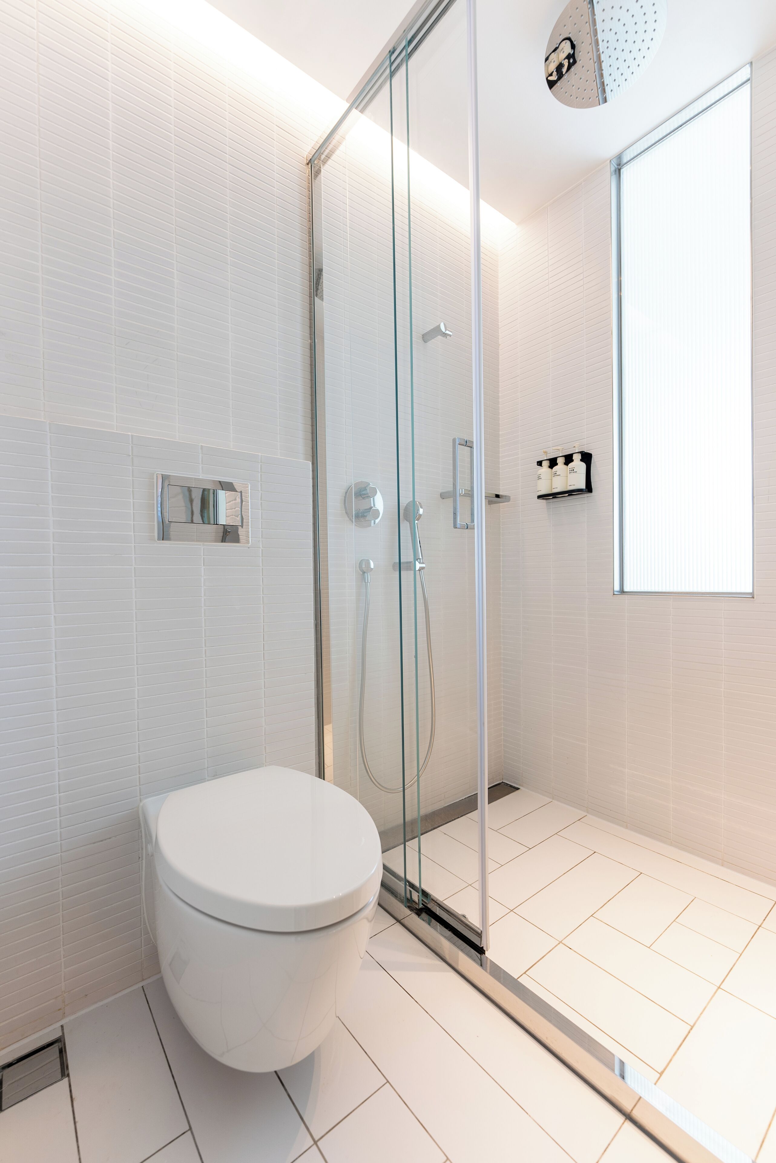 Ein modernes Badezimmer mit einer gläsernen Duschkabine, einer weißen Toilette und einem gefliesten Boden.