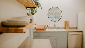 Une cuisine équipée d’un évier, d’étagères en bois, d’un miroir et d’une plante.