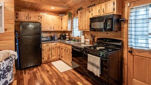 Una cocina estilo cabaña con armarios de madera, un refrigerador negro, un microondas, una estufa y un lavamanos.