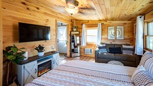 Un acogedor interior de cabaña de madera con chimenea, un sofá, una cama y un televisor.