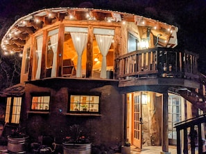 A rustic wooden building with a balcony, large windows, and string lights.